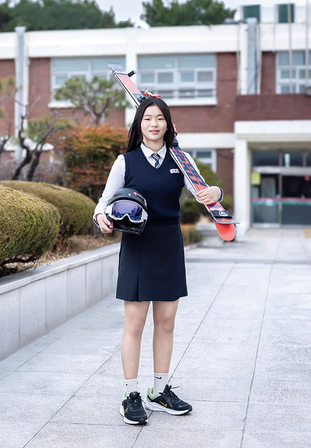 신혜오 선수가 스키와 헬멧을 들고 환하게 웃고 있다.